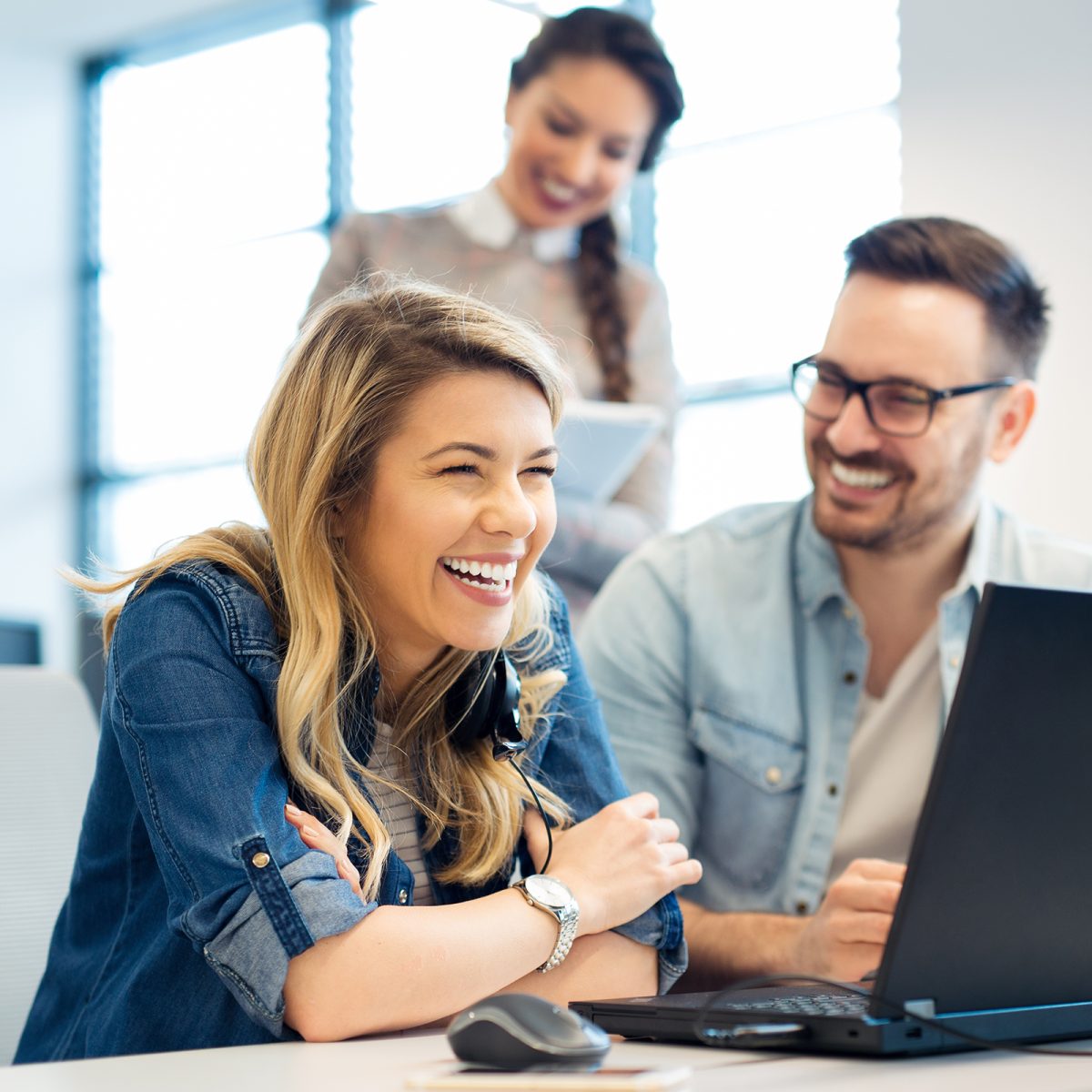 three people laughing and smiling, while a laptop is open in front of them